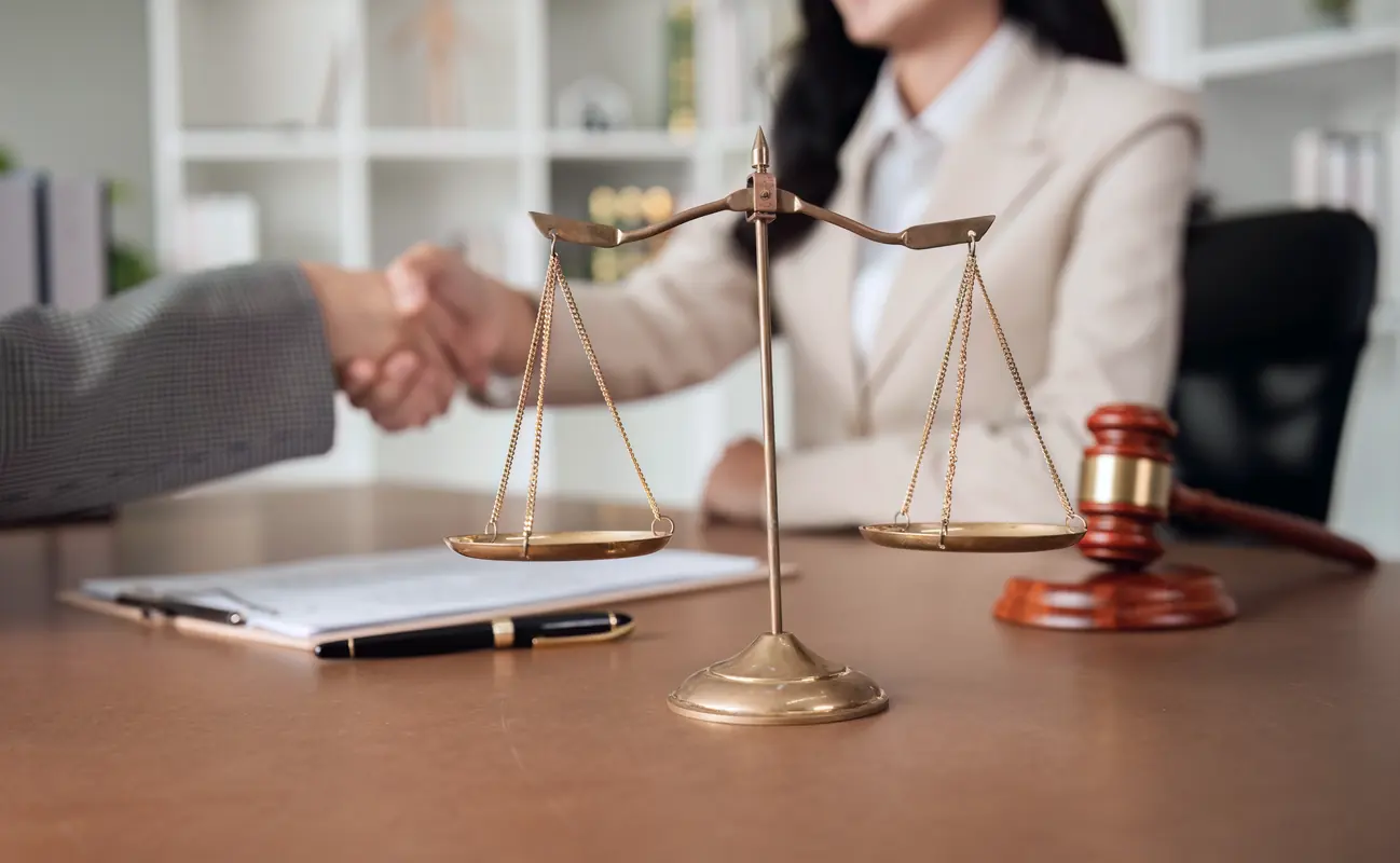 Two professionals shaking hands beside a brass scale of justice
